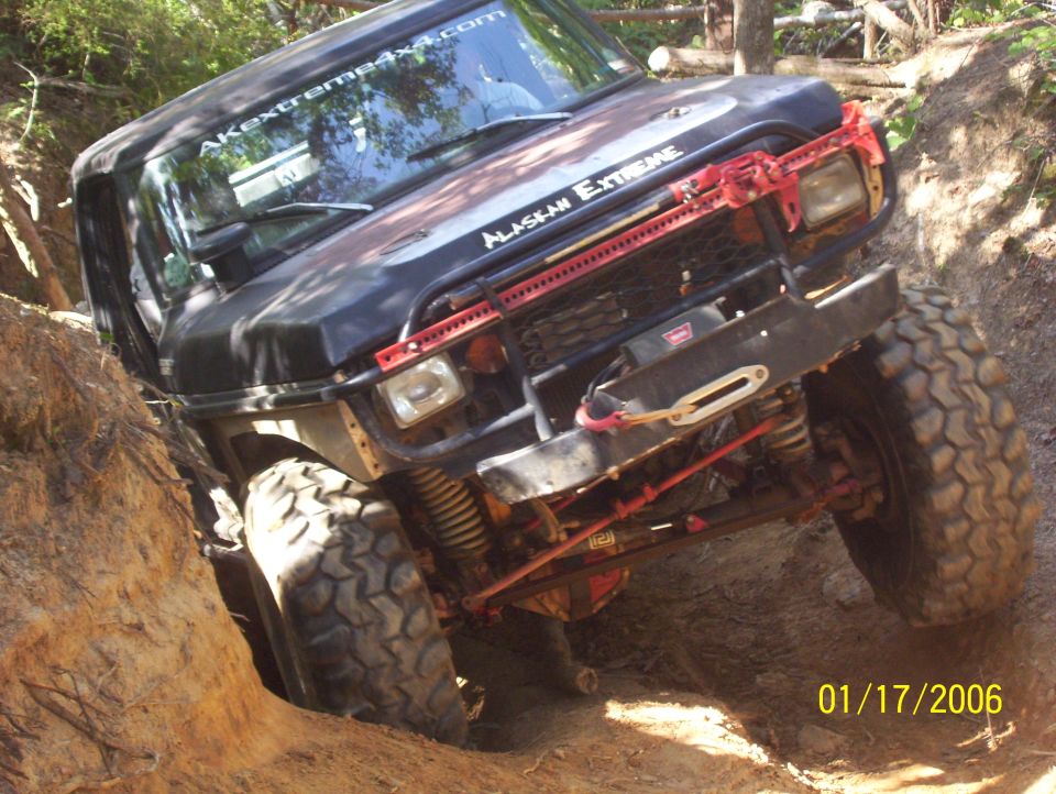 Off-road vehicle with large tires navigating a dirt trail, has 'AKEXTREME4X4.COM' on windshield