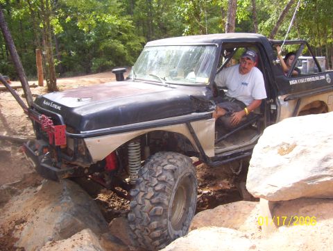 1978 Ford Bronco - A heavily modified pickup truck is shown off-roading over large rocks on a trail.