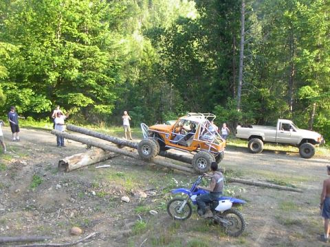 1988 Ford Bronco - Several people watch as an off-road buggy navigates a log obstacle course in a wooded area.