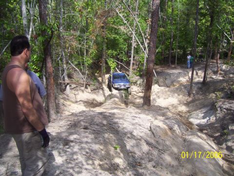 1978 Ford Bronco - A blue SUV tackles an off-road trail in a wooded area.
