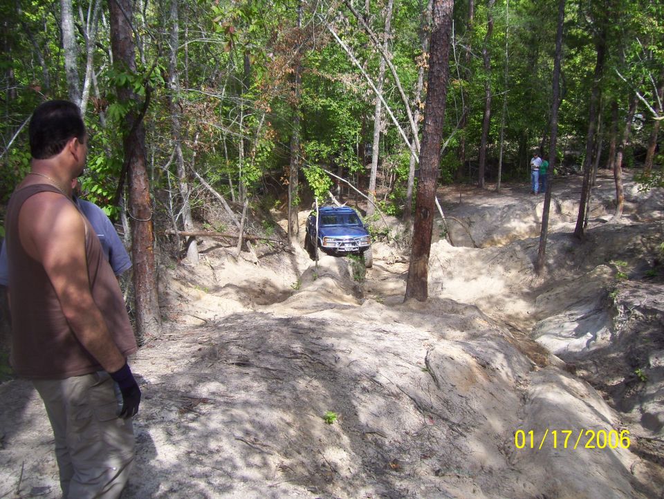 Blue SUV navigating a steep dirt path with trees on either side