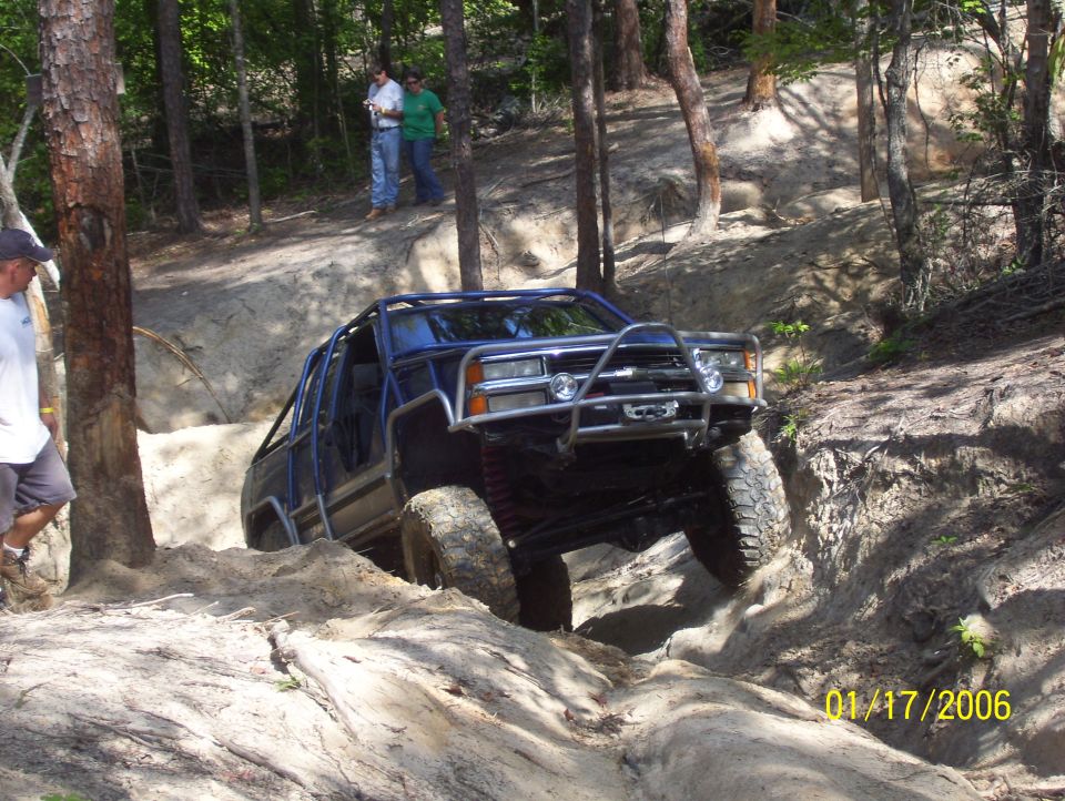 Blue off-road vehicle with roll cage navigating a dirt trail