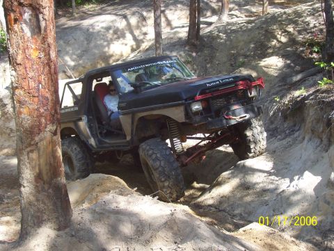 1978 Ford Bronco - Modified off-road SUV tackles a steep dirt incline with large tires and a roll cage.