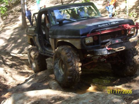 1978 Ford Bronco - This heavily modified off-road vehicle navigates a challenging muddy and rocky terrain, with "ALASKAN EXTREME" visible on its hood.