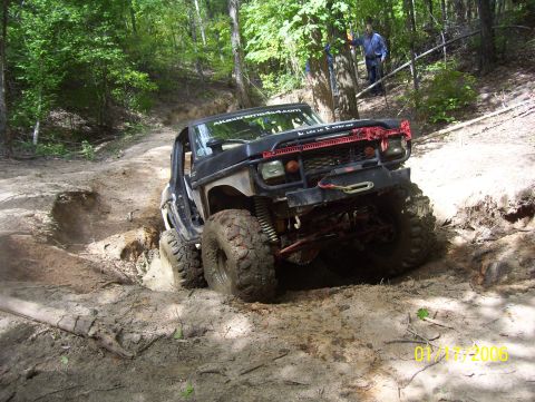 1978 Ford Bronco - This modified off-road vehicle is tackling a challenging muddy terrain with large tires and a winch.