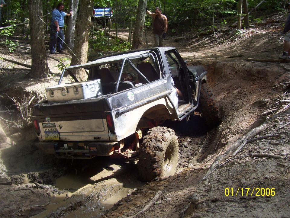 1978 Ford Bronco off-roading through mud, driver's door open, roll cage installed