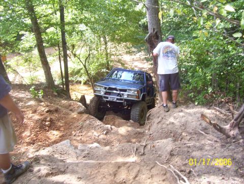1978 Ford Bronco - Off-road SUV tackles a challenging dirt trail surrounded by dense woods.