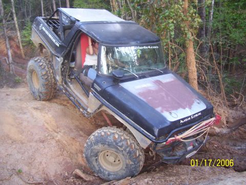 1978 Ford Bronco - This heavily modified SUV is navigating a challenging off-road trail with steep inclines and muddy terrain.