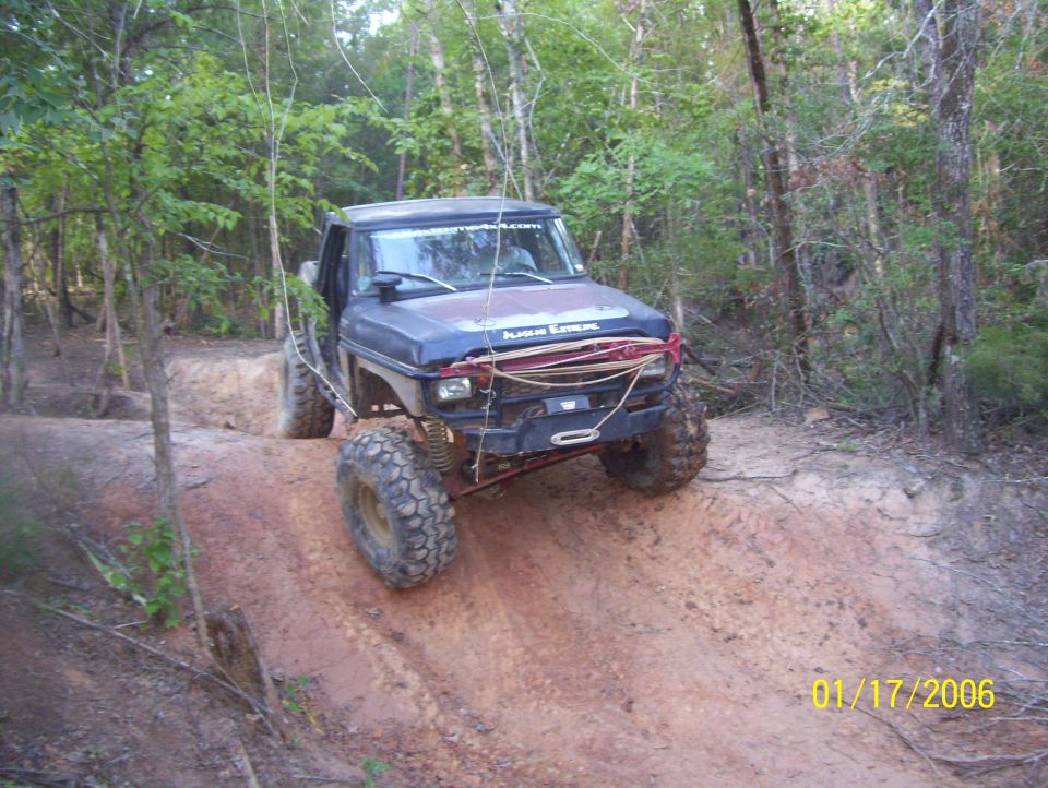 Dark blue off-road vehicle with large tires on a dirt trail, front bumper modified with winch and tow hooks