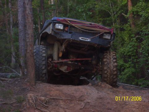 1978 Ford Bronco - An off-road vehicle navigates a steep, muddy trail surrounded by trees.