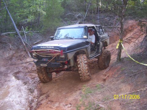1978 Ford Bronco - This modified off-road vehicle is shown on a challenging muddy track with trees and foliage in the background.