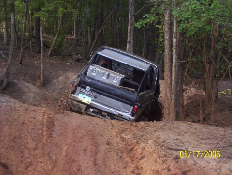 1978 Ford Bronco - A black 1978 Ford Bronco is shown at an extreme angle, stuck in a muddy ditch in a wooded area. The vehicle has a silver toolbox mounted in…