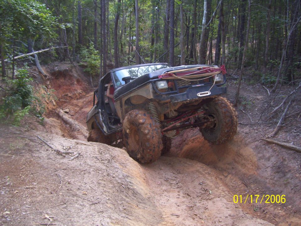 Lifted black Ford Bronco off-roading on a steep, muddy trail in a forest.