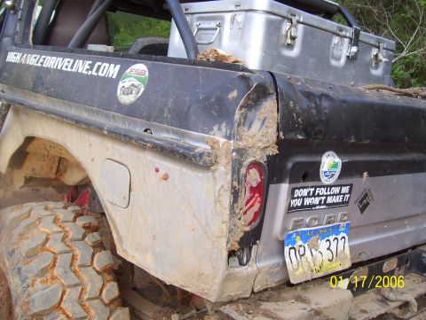1978 Ford Bronco - The rear quarter panel of a mud-covered Ford Bronco is shown, featuring a dented fender, a broken taillight, and various stickers. A licens…
