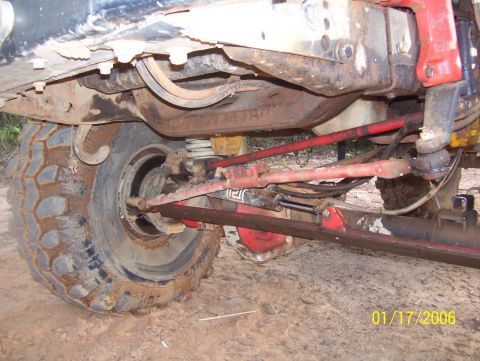 1978 Ford Bronco - Close-up view of the undercarriage of a modified 1978 Ford Bronco, focusing on the front wheel, suspension, and steering components. The ve…