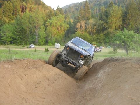 1988 Ford Bronco - An SUV navigates a challenging off-road course, with trees and hills in the distance.