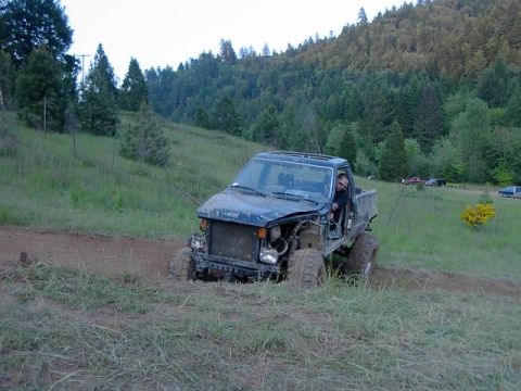 1988 Ford Bronco - This heavily modified off-road truck navigates a muddy trail through a grassy, wooded area.