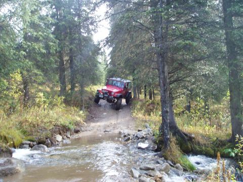 2000 Ford E350 - A red Jeep Wrangler navigates a rocky stream crossing on a wooded trail.