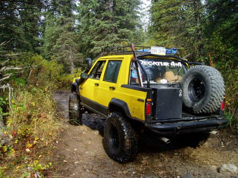 2000 Ford E350 - Yellow Jeep Cherokee XJ navigates a muddy forest trail, equipped for off-road adventure.
