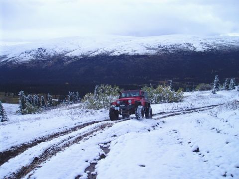 2000 Ford E350 - A red Jeep navigates a snow-covered trail through a wooded mountain landscape.