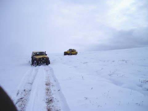 2000 Ford E350 - Two yellow off-road vehicles navigate a snow-covered terrain under an overcast sky.