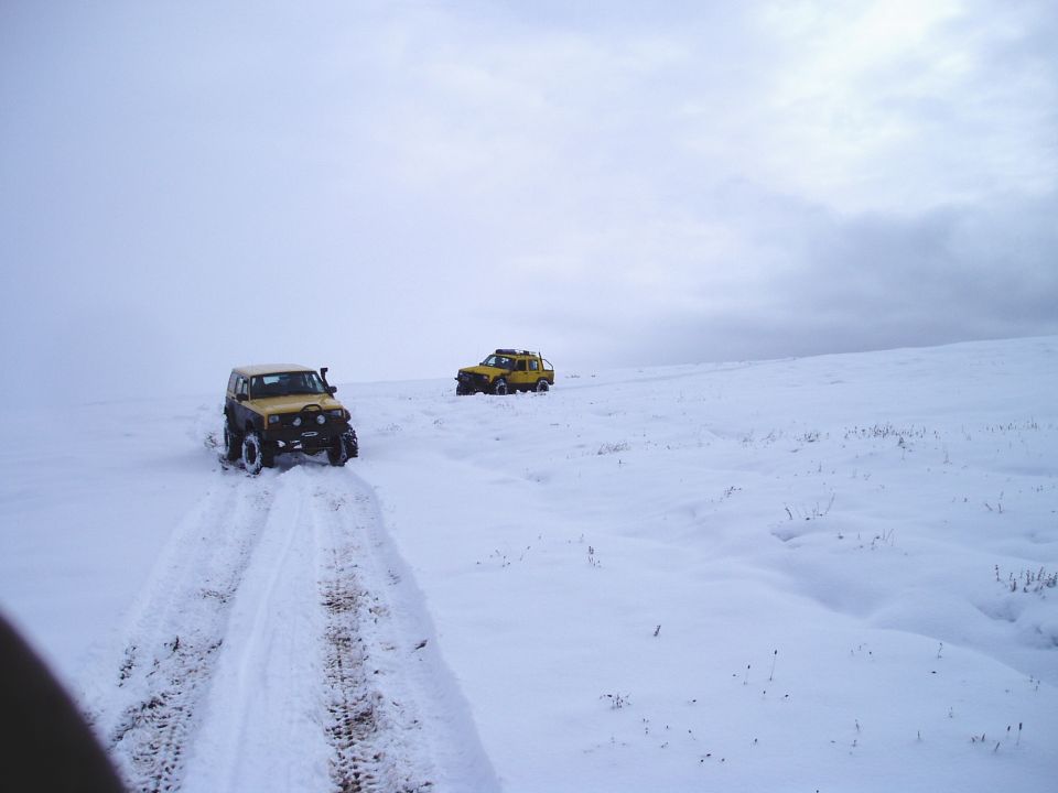 Two yellow off-road vehicles driving on a snowy landscape