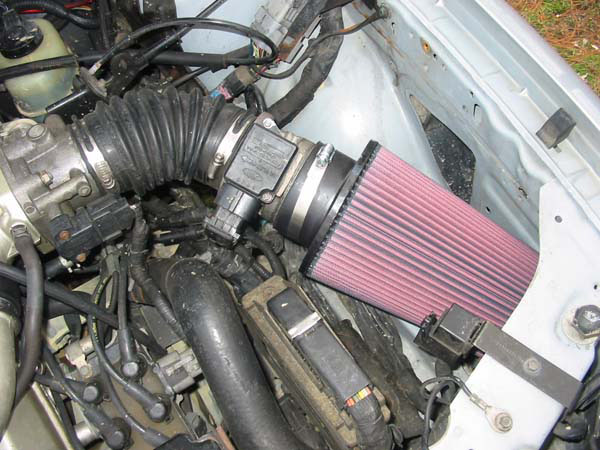 Engine bay with aftermarket red cone air filter intake attached to MAF sensor and accordion hose