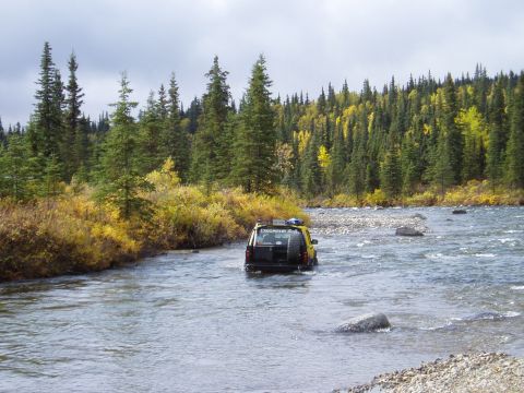 2000 Ford E350 - A yellow SUV navigates a rocky riverbed surrounded by dense forest and autumn colors.
