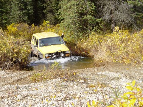 2000 Ford E350 - Off-road SUV navigates a water crossing surrounded by autumn foliage.