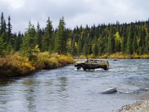 2000 Ford E350 - A Jeep Cherokee XJ navigates a river in a wooded area during autumn.