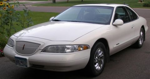 1998 Lincoln Mark VIII - A white coupe sits parked on a paved surface in front of a residential home, with sunflowers to the left.