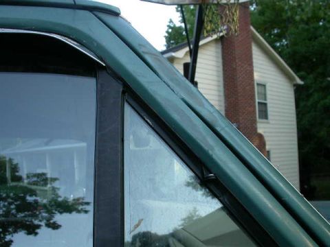 1990 Ford Bronco - A partial view of a green vehicle's door frame is shown with a house and chimney in the background.