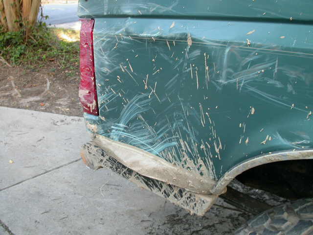 Green 1990 Ford Bronco rear quarter panel covered in mud with a dented bumper