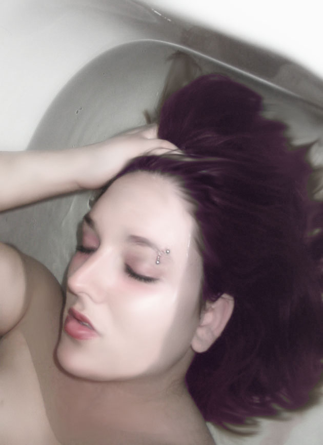 Woman with dark hair lying in a bathtub, eyes closed, hand on head