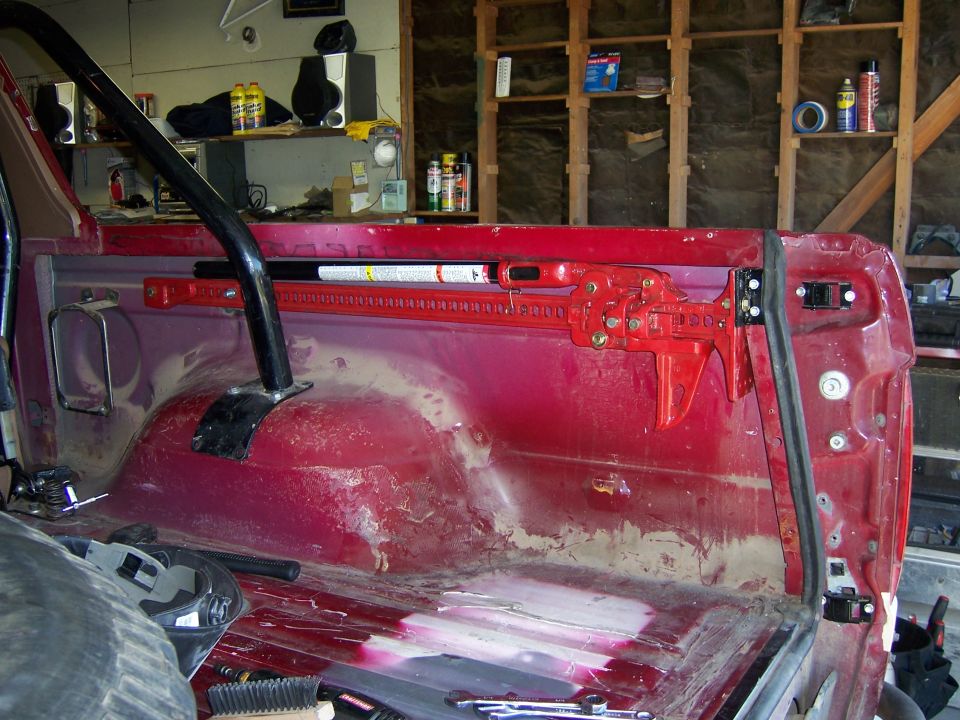 Red interior of a vehicle with a high lift jack mounted on the side panel. Roll bar visible