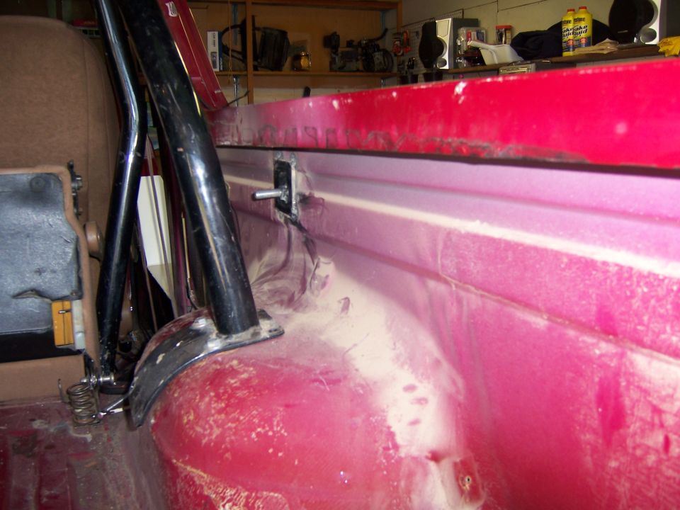 Close-up of a black roll cage mounting bracket bolted to the red interior of a vehicle