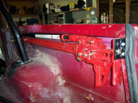 1991 Ford Bronco - A red high lift jack is mounted inside the vehicle, secured to the side panel with a bracket.