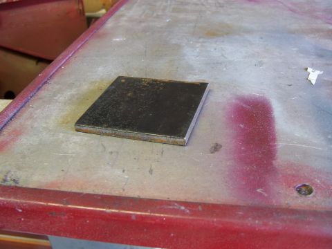 1991 Ford Bronco - A close-up view of a metal plate resting on a workbench with some red paint visible.
