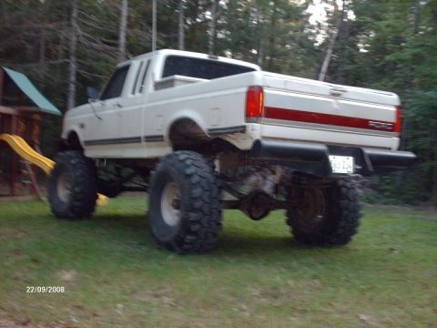 1990 Ford F-150 - This lifted 1990 Ford F-150 pickup truck features a white body with red stripe accents and oversized off-road tires.