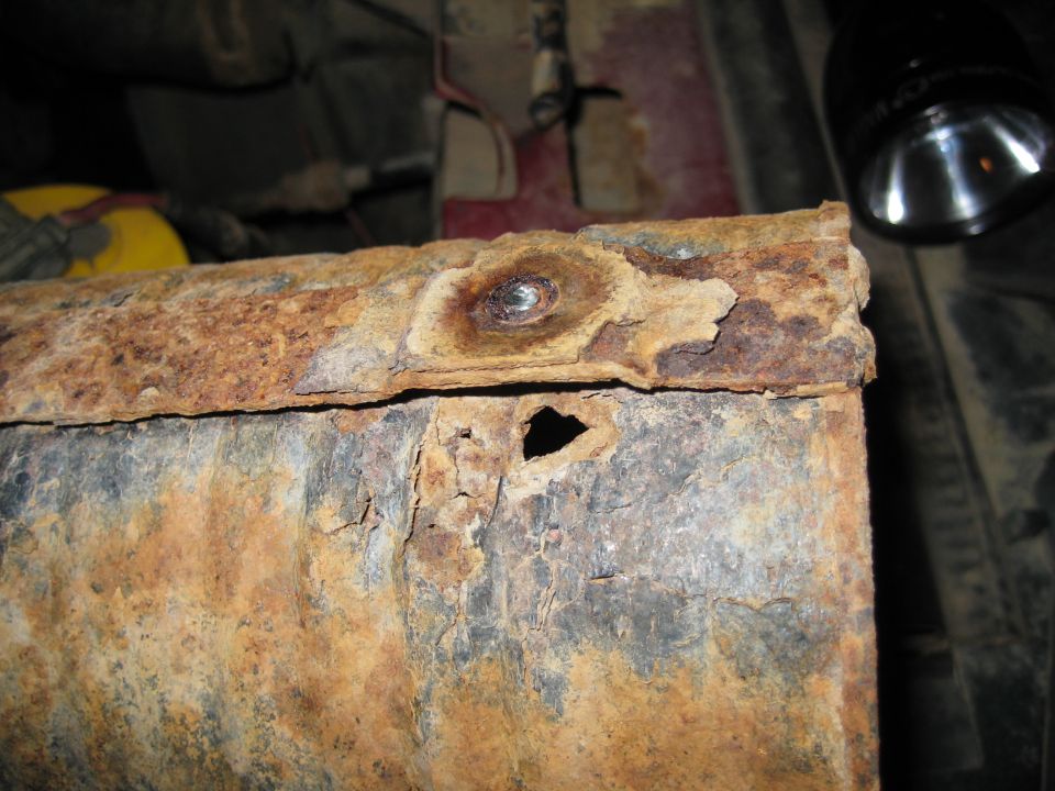 Heavily rusted metal frame with a hole and a bolt head visible