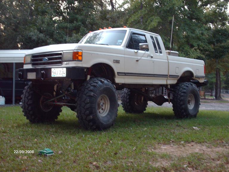 White 1990 Ford F-150 pickup truck with large tires and a lift kit, parked on grass