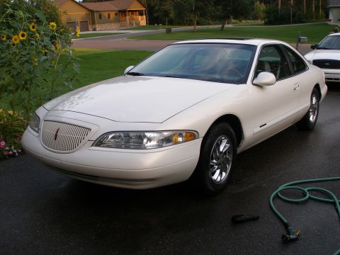 1998 Lincoln Mark VIII - A white 1998 Lincoln Mark VIII coupe is parked on a wet driveway next to a house.