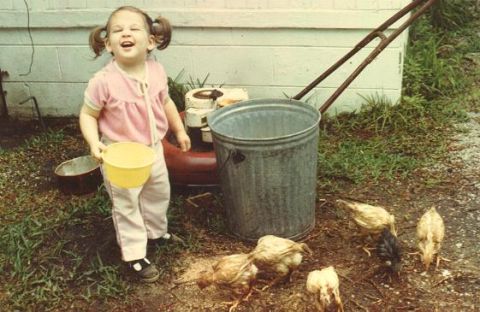 1994 Ford Taurus - A young child stands with chickens near a lawnmower and trash can.