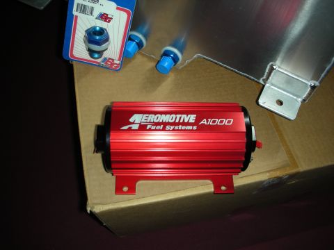 1998 Ford Crown Victoria - A red anodized Aeromotive A1000 fuel pump on its mounting bracket, sitting on a cardboard box next to a welded aluminum fuel cell or tank w…