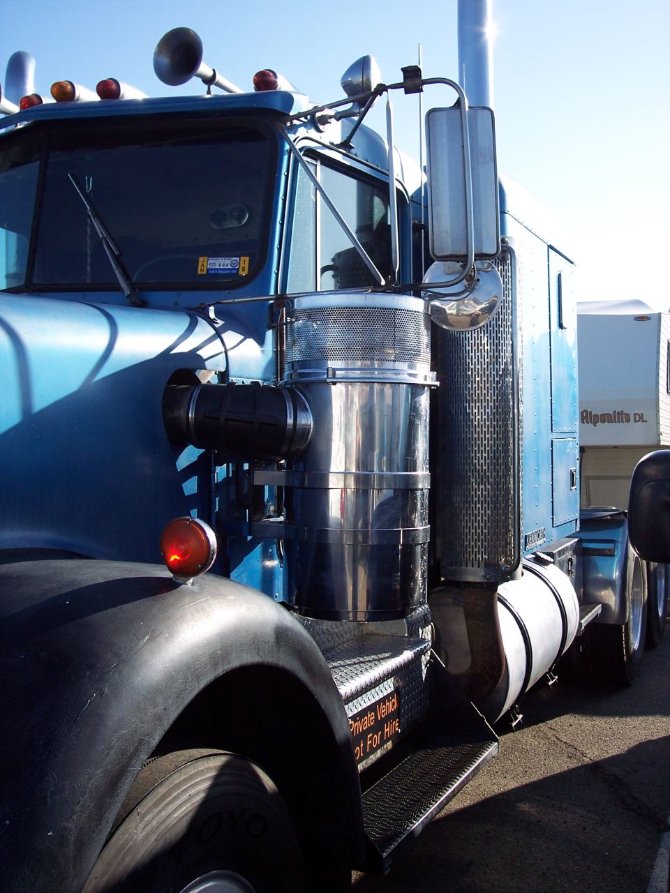 Driver side of blue Kenworth semi truck with chrome stack and air cleaner