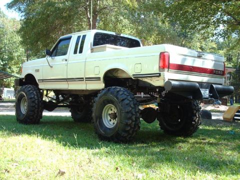 1990 Ford F-150 - This lifted 1990 Ford F-150 pickup truck sits on a grassy area with trees in the background.