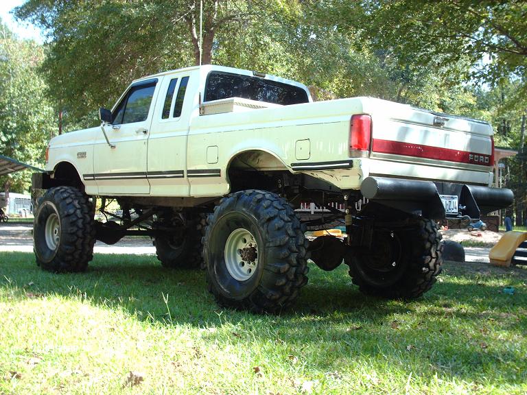 White 1990 Ford F-150 pickup truck with large off-road tires and lifted suspension, viewed from the rear