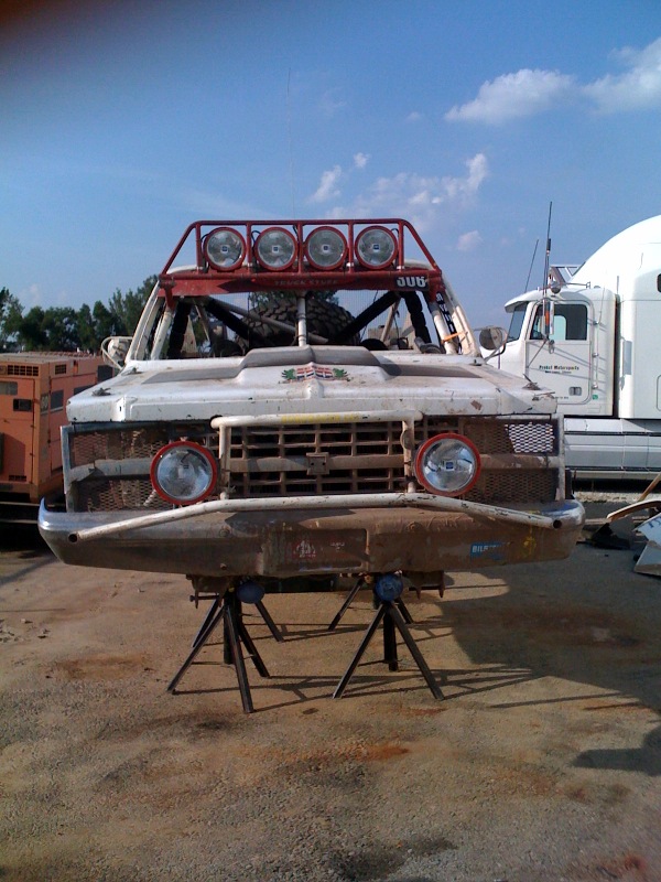 Front view of weathered off-road race truck with roof light bar on jack stands
