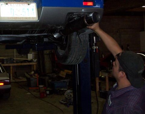 1988 Pontiac Fiero - A person works on the exhaust system of a blue car lifted on a mechanic's hoist.