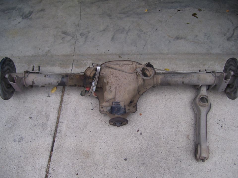 Removed solid rear axle assembly with differential, drum brake plates, and a control arm on concrete